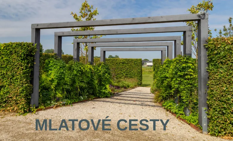 Ukončená mlatová cesta s kamenným povrchem, živými ploty a dřevěnými oblouky.