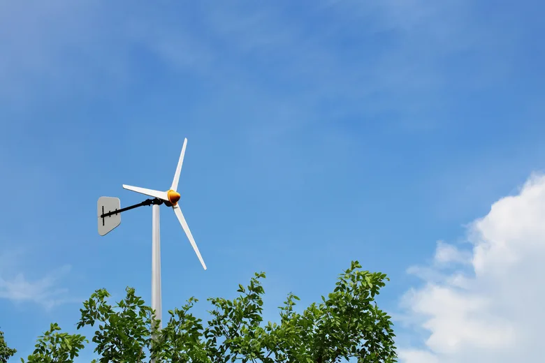 Malá domácí větrná elektrárna na sloupě pod modrou oblohou.