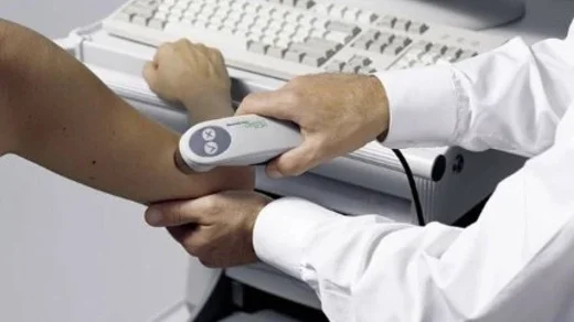 Lékař zkoumá paži pacienta pomocí diagnostického přístroje.