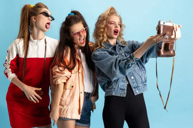 Tři ženy v módních outfittech dělají selfie starým fotoaparátem.
