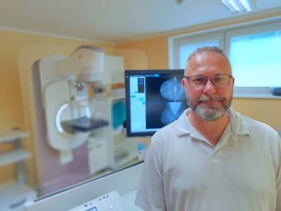 Muž stojí v ordinaci vedle mamografu pro vyšetření prsu.