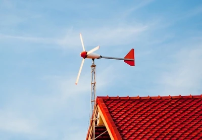 Malá větrná elektrárna na střeše domu pod modrou oblohou.