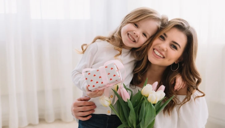 Matka s dcerou drží kytici tulipánů v jasném interiéru.