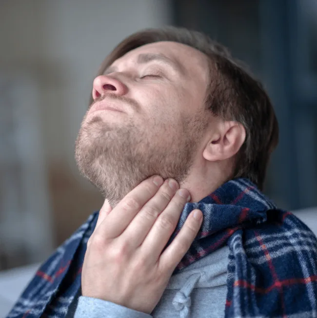 Muž s bolestmi v krku drží si ruku na hrdle.