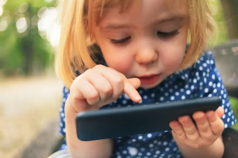 Malá holčička se soustředěně dívá na tablet venku.