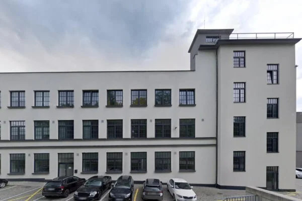 Bílá budova s okny a parkovanými auty před ní.