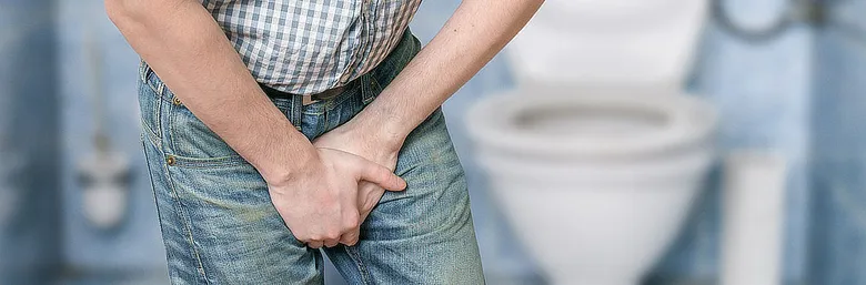 Muž drží varlata v bolesti na záchodě.