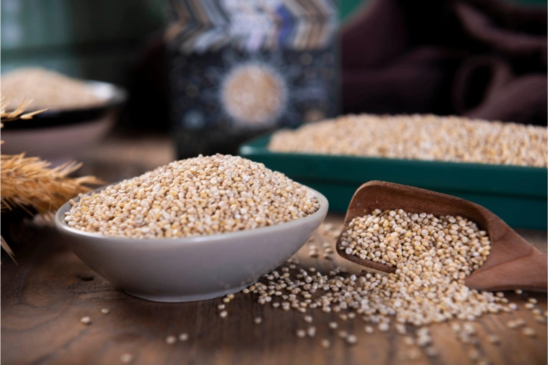 Quinoa zrny v misce na dřevěném stole s lžící.