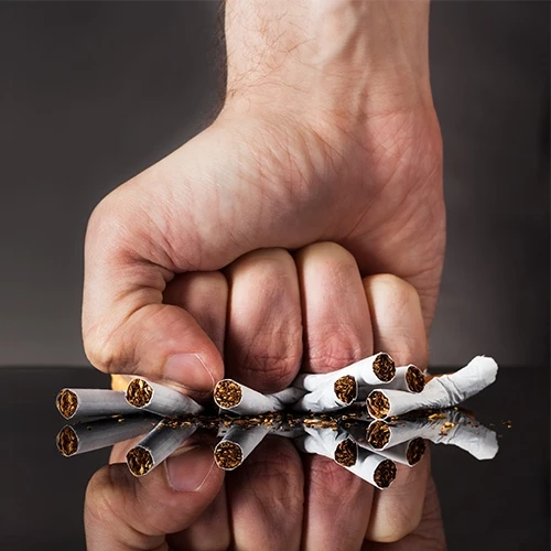 Mužova pěst rozbíjí cigarety jako metafora pro přestání s kouřením.