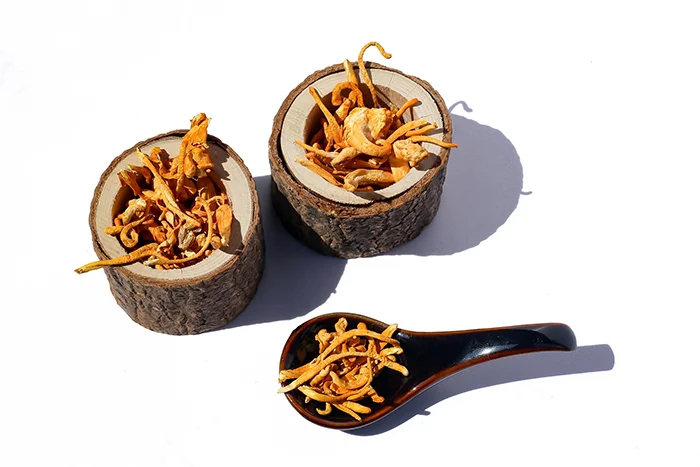 Sušené houby cordyceps v dřevěných miskách na bílém pozadí.