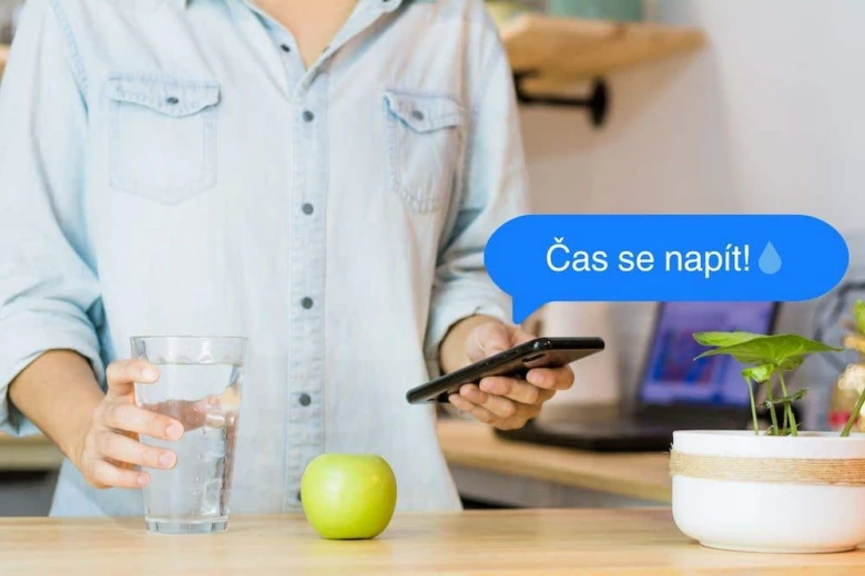 Člověk s sklenicí vody, jablkem a rostlinou na stole.