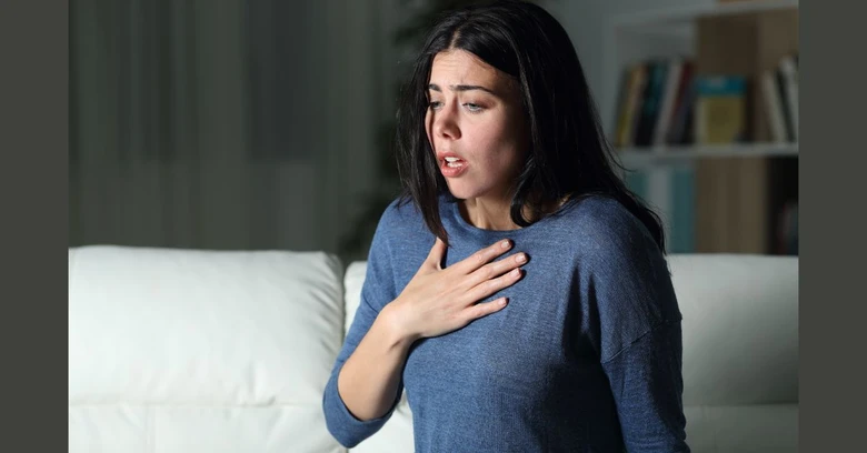Žena s rukou na hrudi při hyperventilaci v interiéru.