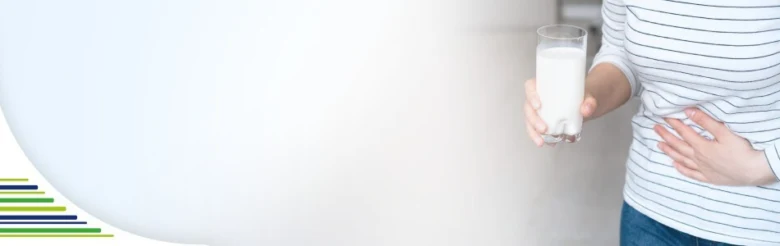 Žena drží sklenici mléka a tlačí si na břicho kvůli trávicím problémům.