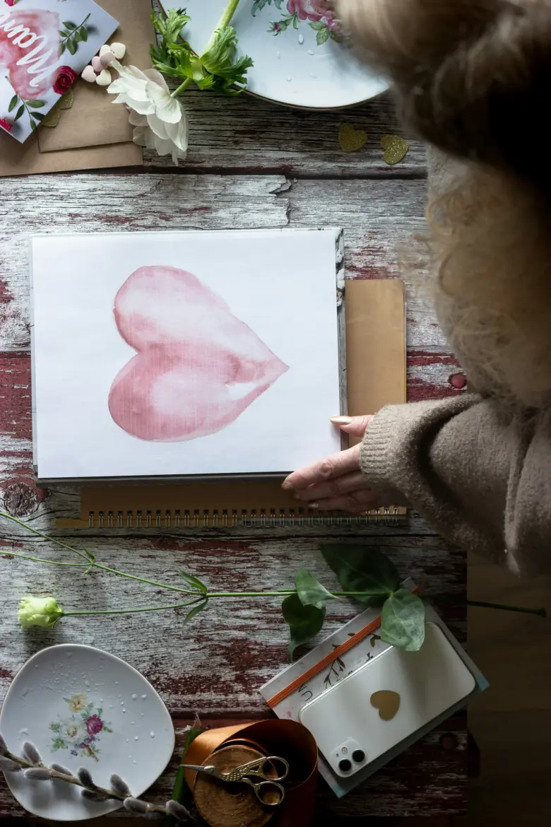 Stůl s valentýnskými dekoracemi, květinami a řemeslnými předměty.