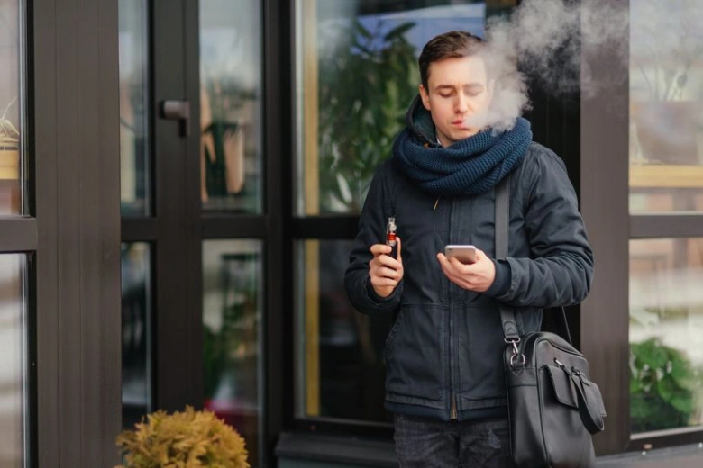 Muž stojí venku a vapuje s elektronickou cigaretou.