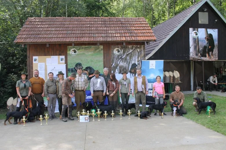 Skupina lidí s slovenskými kopovy před dřevěnou budovou venku.