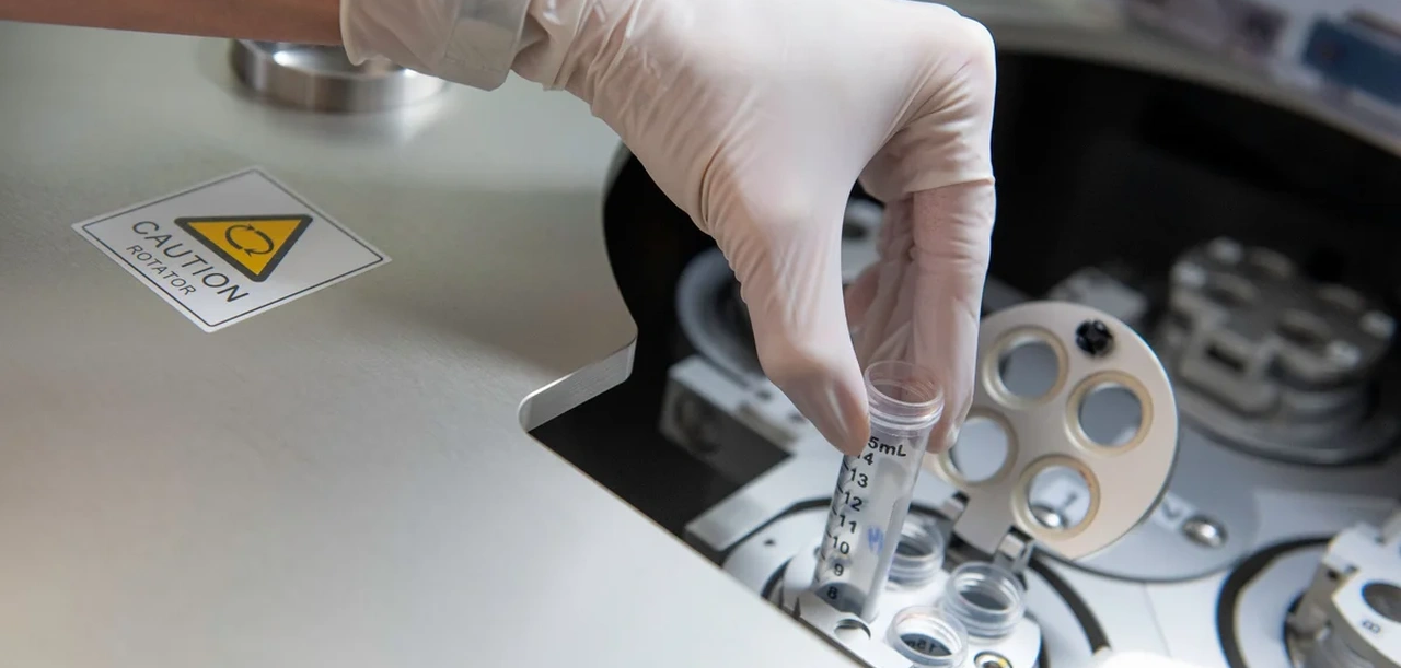 Ruka v rukavici vkládá zkumavku do laboratorního rotátoru.