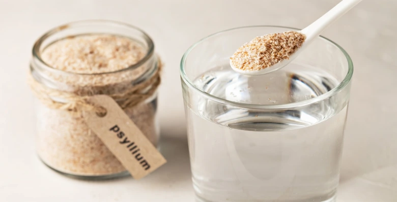 Lžíce s psylliem nad sklenicí vody vedle lahvičky označené psyllium.