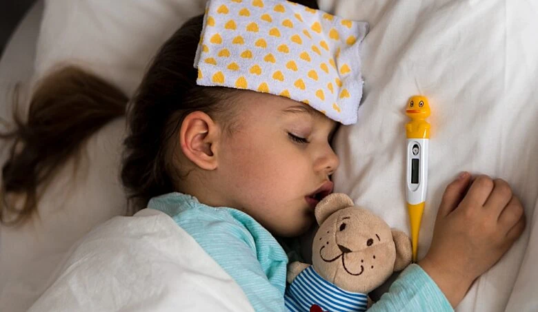 Spící nemocná dívka s teploměrem na posteli.