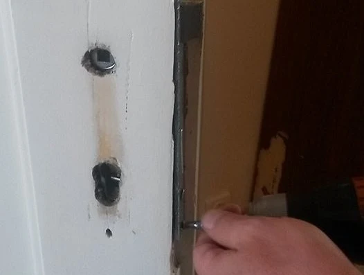 Ruka šroubuje mechanismus zámku do dveřního rámu.