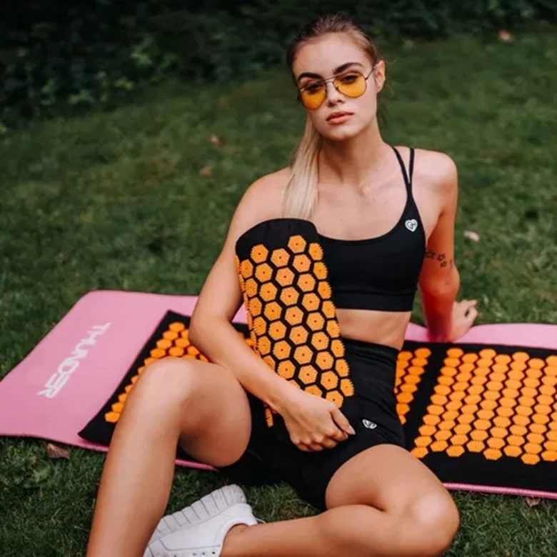 Žena sedí na trávě s akupresurním válcem pro relaxaci.