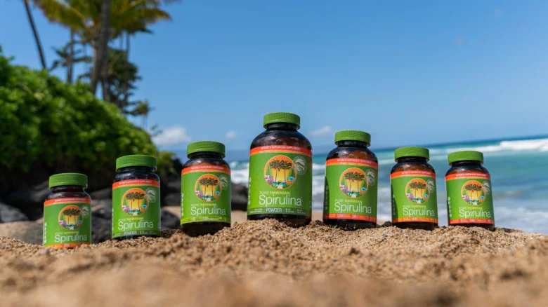Fľaše spiruliny na pláži s oceánem v pozadí.
