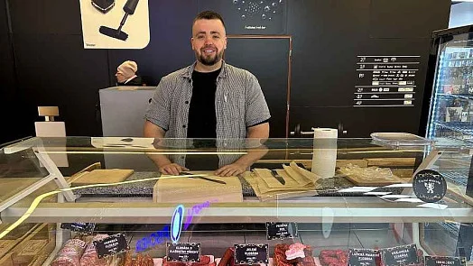 Muž stojí za pultem v obchodě s potravinami.