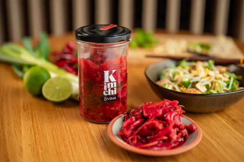 Sklenice fermentovaného kimbáče s čerstvými zeleninovými ingrediencemi.