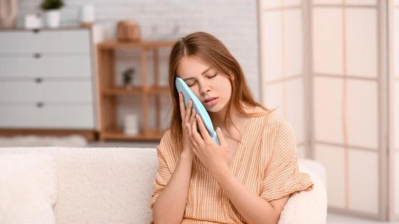 Žena sedí na gauči s ledovým obkladem pro úlevu od bolesti.