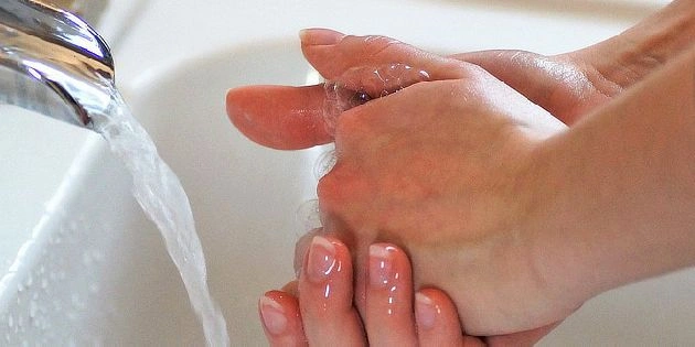 Člověk si umývá ruce pod tekoucí vodou v dřezu.