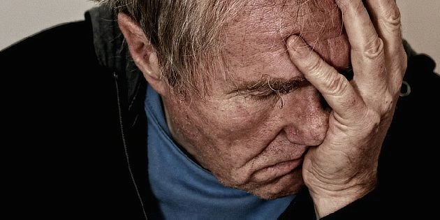 Muž drží hlavu v rukou a vypadá smutně.