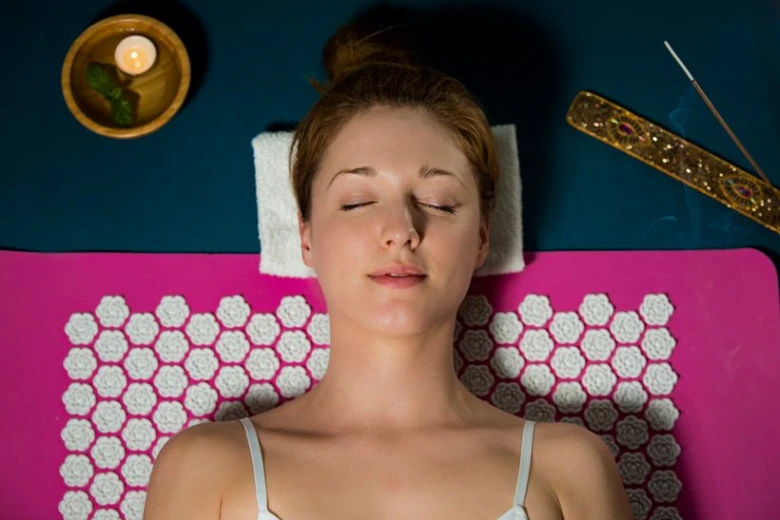 Žena leží na akupresurní podložce v relaxačním prostředí.