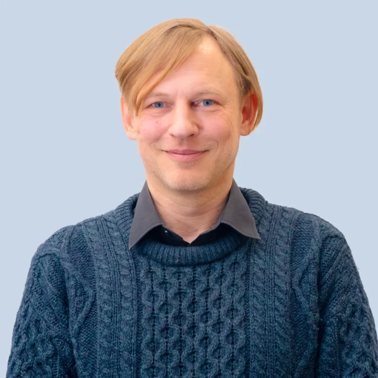 Muž v modrém svetrku na světlom pozadí.