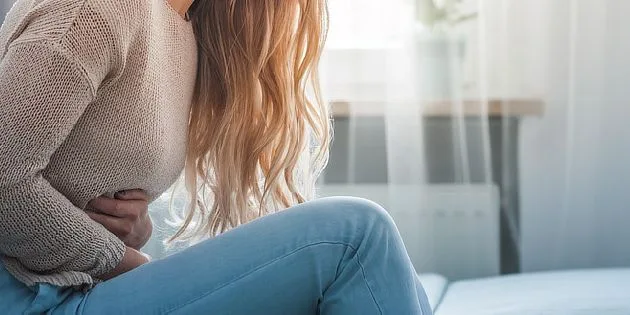 Žena drží břicho v bolesti uvnitř světlé místnosti.