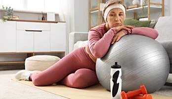 Žena v sportovním oblečení odpočívá na fitbalu.