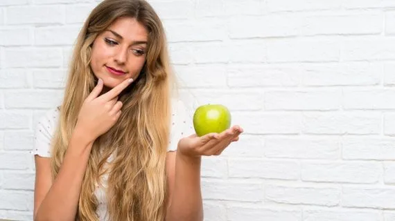 Mladá žena drží zelené jablko v ruce před bílou zdí.