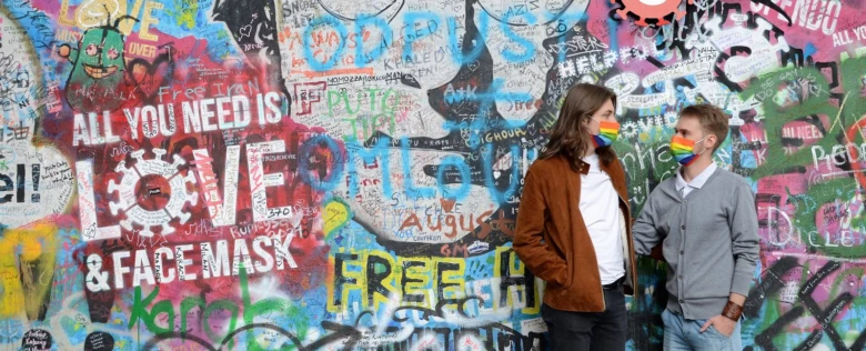 Dvě osoby s deštníkovými rouškami před grafitovou zdí.
