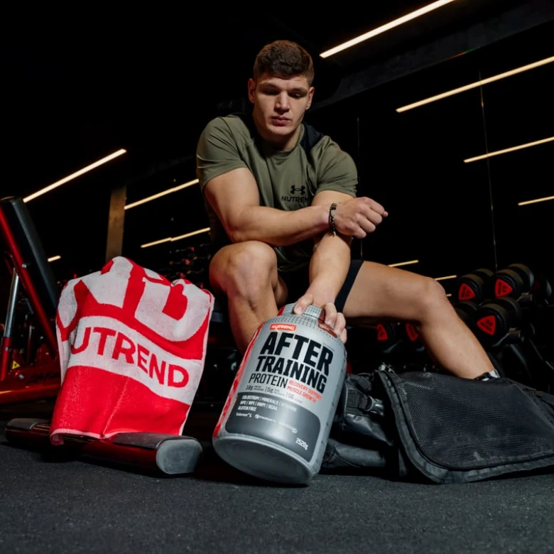 Muž v posilovně s nádobou proteínového prášku pro sportovce.
