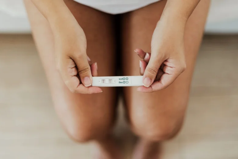 Žena drží v rukou pozitivní těhotenský test s dvěma čarami.