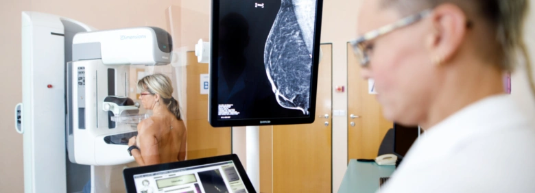Žena podléhá mamografii, lékař sleduje výsledky na obrazovce.
