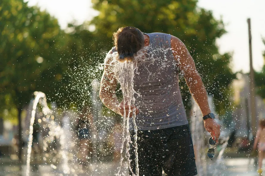 Muž se ochlazuje ve veřejném fontánu v horkém červnovém dni.