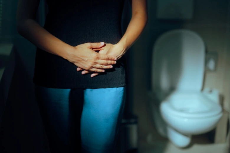 Žena drží břicho v koupelně u toalety s příznaky hyperaktivního močového měchýře.