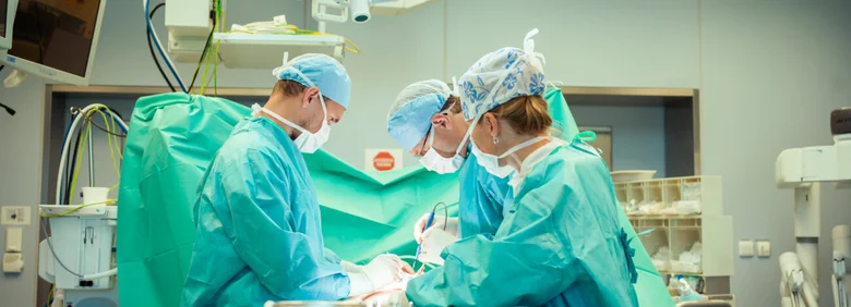 Tři chirurzi operují pacienta v operační sále.