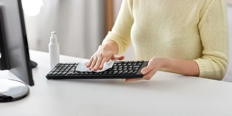 Osoba čistí počítačovou klávesnici na bílém stole.