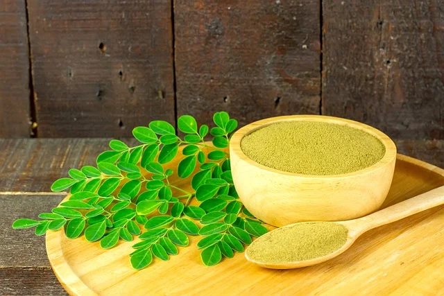 Moringa prášek v dřevěné misce s čerstvými listy.