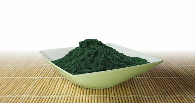 Bílá miska s tmavě zelenou práškovou spirulinou na bambusové podložce.