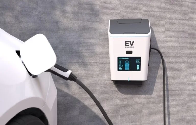 Bílý elektromobil nabíjen na zdi uvolněným kabelovým adaptérem.