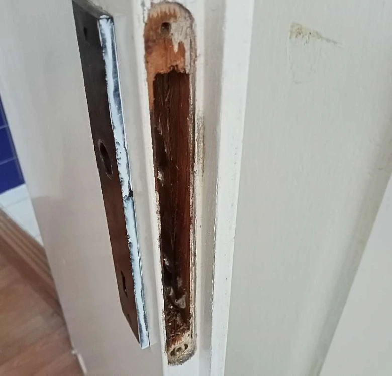 Poškozený dřevěný úderový prvek pro zadlabací zámek na dveřním rámu.