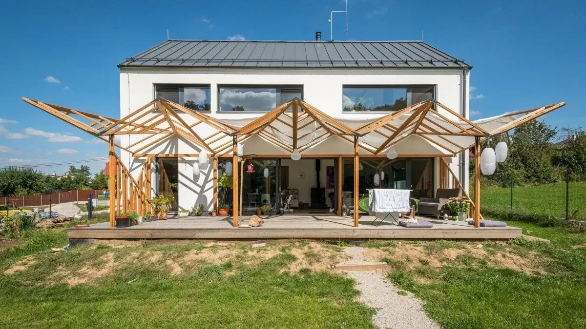 Dřevěná pergola bez hřebíků před bílým domem na trávníku.