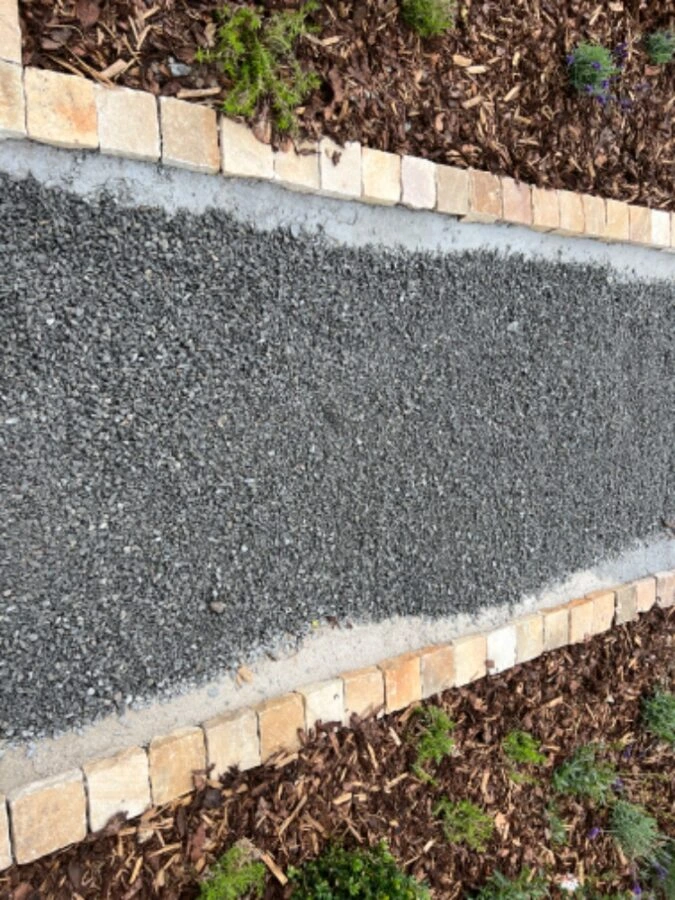 Čerstvě položená štěrková cesta s kamenným lemem a betonovými okraji.